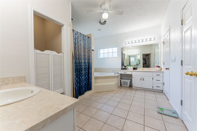 bathroom featuring vanity, a textured ceiling, ceiling fan, a relaxing tiled tub, and tile patterned floors