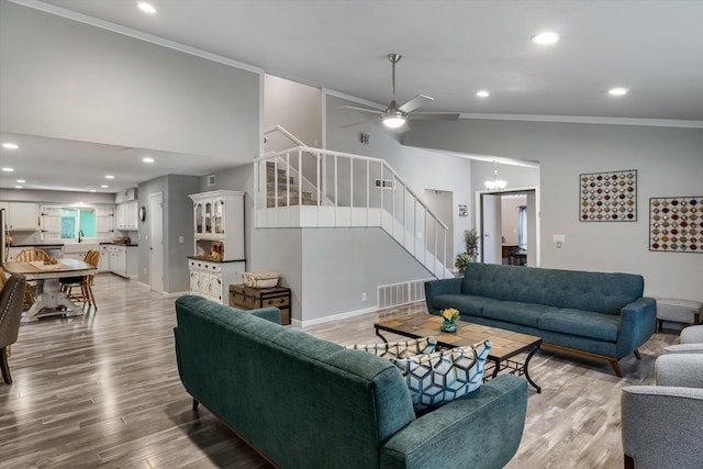 living room featuring ceiling fan with notable chandelier, ornamental molding, lofted ceiling, and light hardwood / wood-style floors