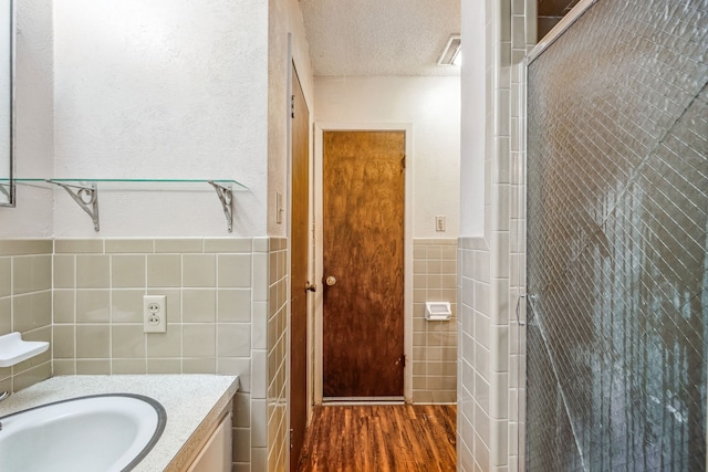 bathroom featuring vanity, a textured ceiling, tile walls, hardwood / wood-style floors, and a shower with shower door