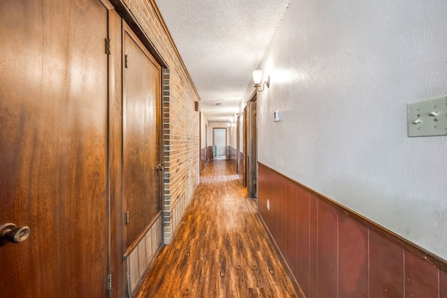 hall featuring a textured ceiling, wooden walls, and dark wood-type flooring