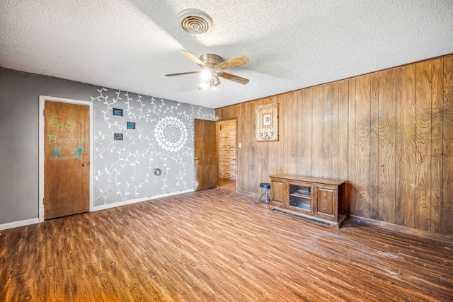 unfurnished living room with wood walls, wood-type flooring, and a textured ceiling