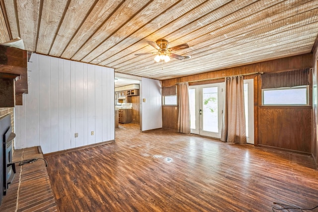 unfurnished living room with wood-type flooring, wood ceiling, ceiling fan, and wood walls