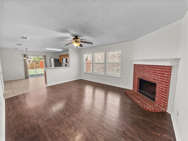 unfurnished living room with a brick fireplace, ceiling fan, a textured ceiling, and light wood-type flooring