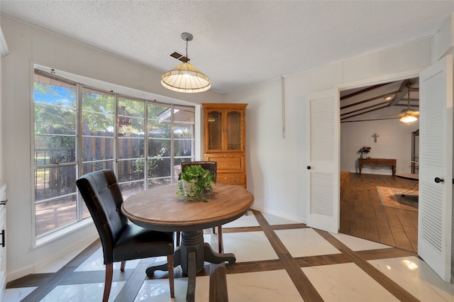 dining area with plenty of natural light, vaulted ceiling with beams, and a textured ceiling