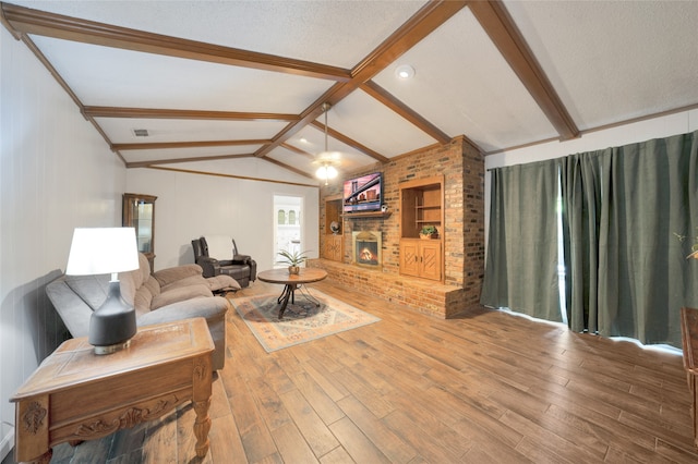 living room with hardwood / wood-style floors, lofted ceiling with beams, a textured ceiling, a brick fireplace, and built in shelves