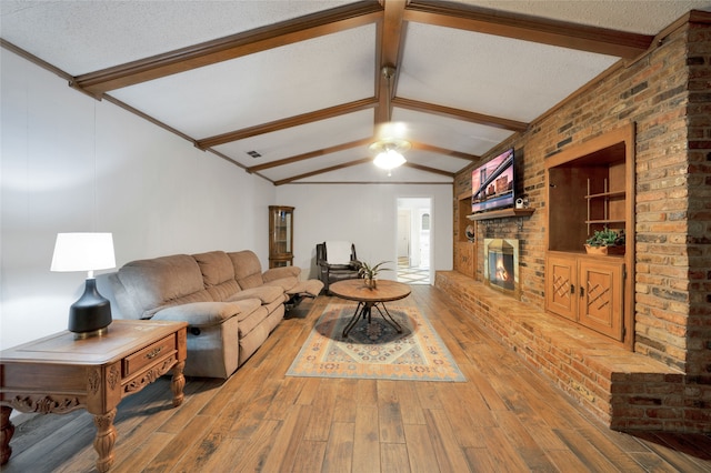 living room featuring vaulted ceiling with beams, hardwood / wood-style flooring, a textured ceiling, and a brick fireplace