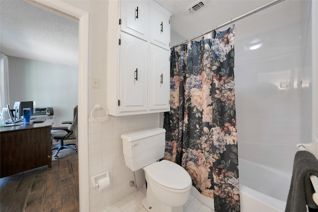 bathroom with tile walls, shower / tub combo with curtain, a textured ceiling, and toilet