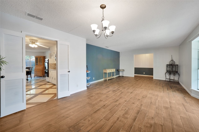 unfurnished living room with ceiling fan with notable chandelier, light wood-type flooring, and a textured ceiling