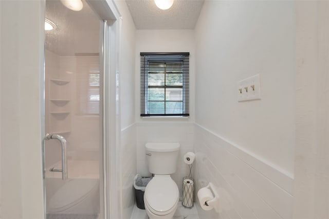 bathroom with tile walls, a textured ceiling, a shower with shower door, and toilet