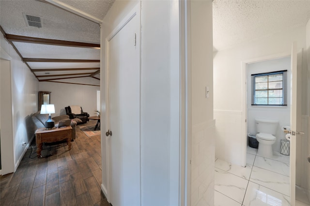 corridor with vaulted ceiling, a textured ceiling, and light wood-type flooring