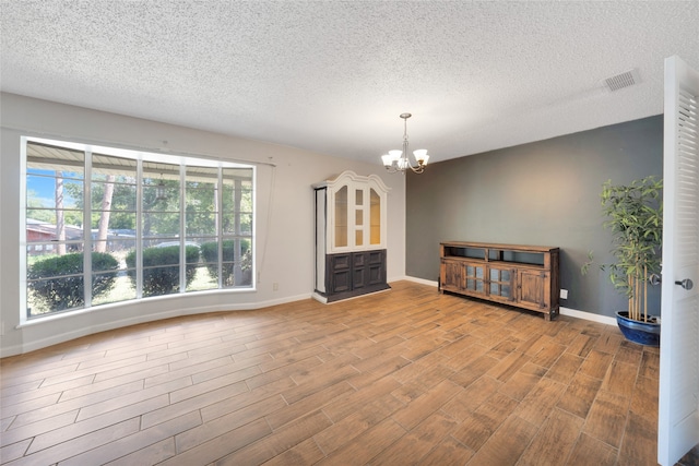 spare room with an inviting chandelier, light hardwood / wood-style flooring, and a textured ceiling