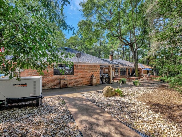 view of front of property featuring roof with shingles, a chimney, a patio, and brick siding