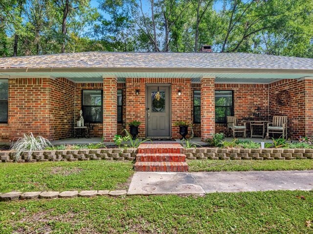 view of exterior entry featuring covered porch and brick siding