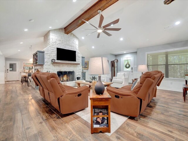 living area featuring vaulted ceiling with beams, a stone fireplace, recessed lighting, wood finished floors, and a ceiling fan