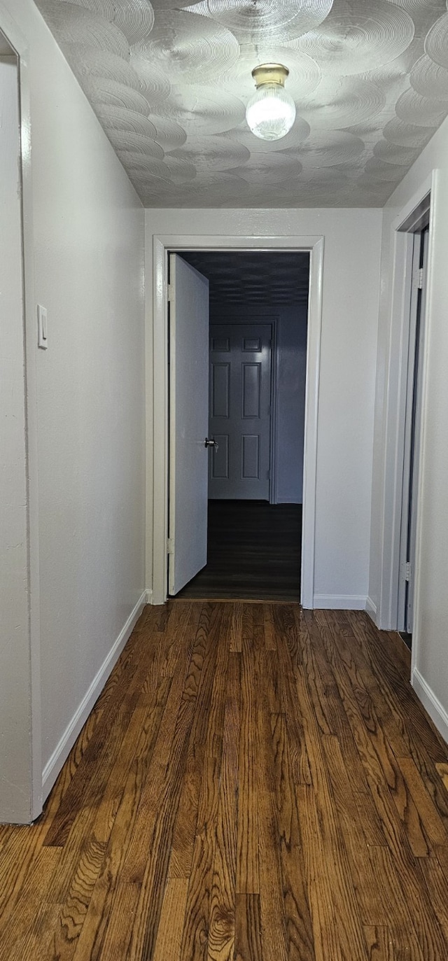 corridor with a textured ceiling and dark hardwood / wood-style floors