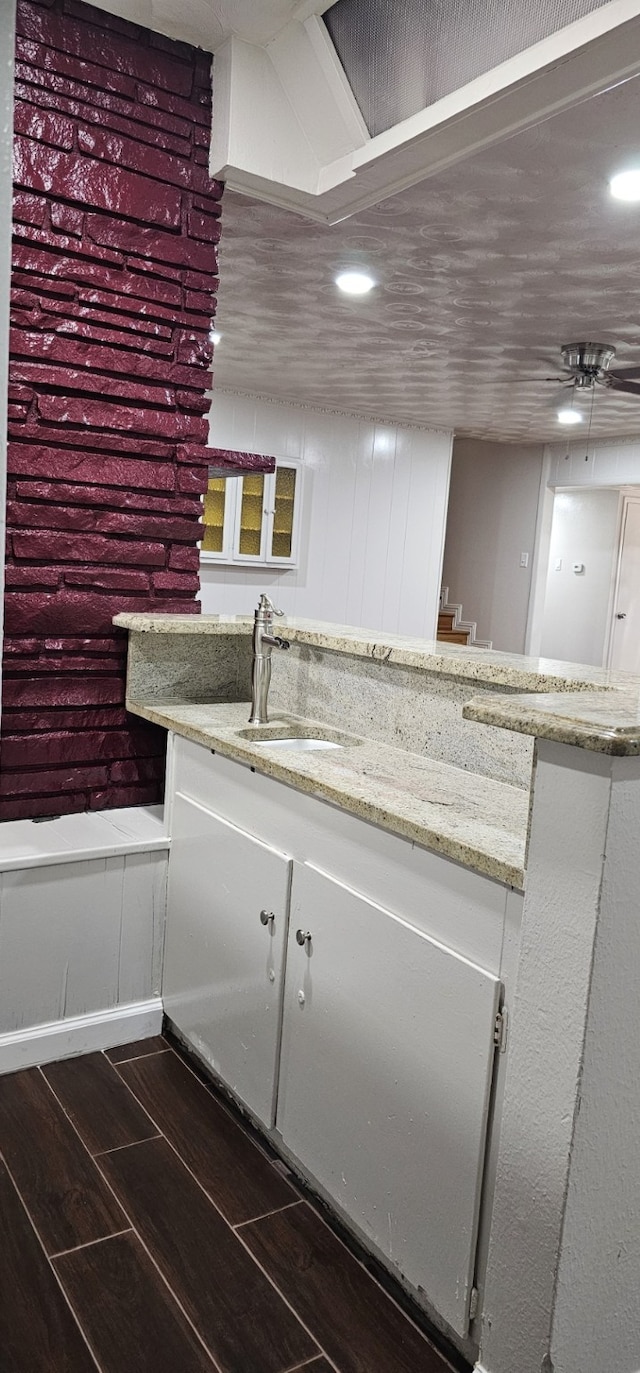 interior space with ceiling fan, sink, light stone countertops, and dark wood-type flooring