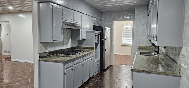 kitchen with stainless steel appliances, dark wood-type flooring, sink, and dark stone counters