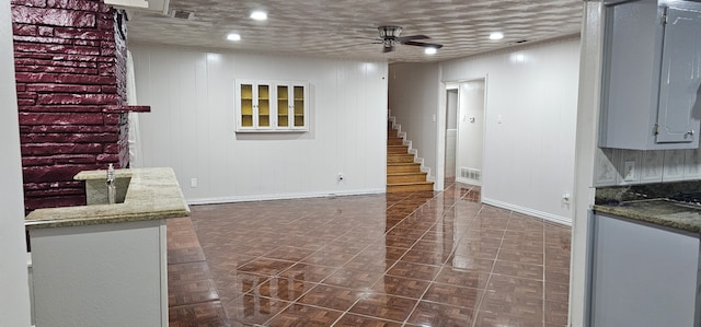 basement with a textured ceiling, ceiling fan, and dark tile patterned flooring