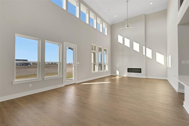 unfurnished living room with ceiling fan, a high ceiling, and light hardwood / wood-style flooring