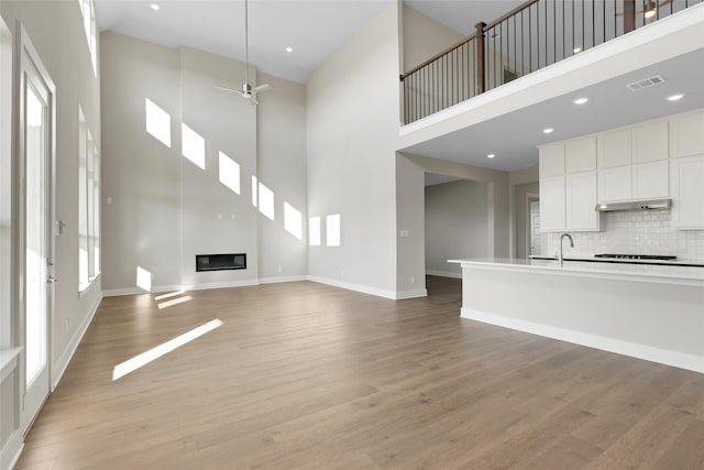 unfurnished living room featuring plenty of natural light, light wood-type flooring, and a towering ceiling