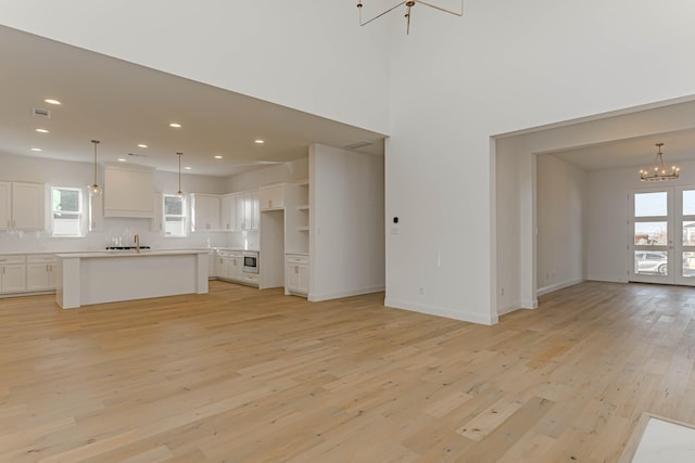 unfurnished living room featuring a notable chandelier, sink, and light wood-type flooring