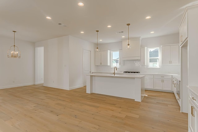 kitchen featuring sink, white cabinetry, light wood-type flooring, an island with sink, and pendant lighting