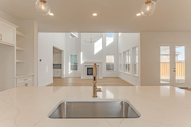 kitchen featuring light stone counters, sink, french doors, and pendant lighting