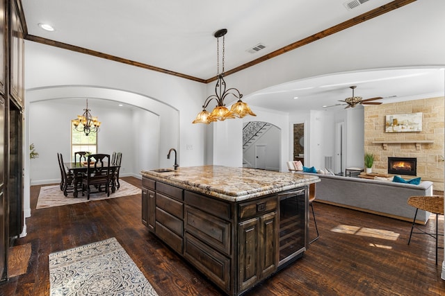 kitchen with an island with sink, sink, beverage cooler, hanging light fixtures, and dark brown cabinetry