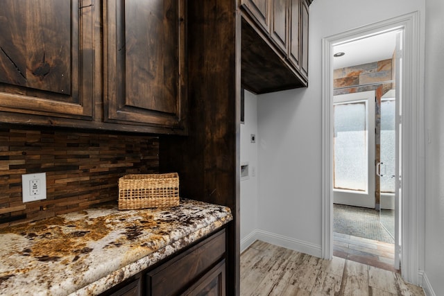 kitchen with light stone counters, decorative backsplash, dark brown cabinets, and light wood-type flooring