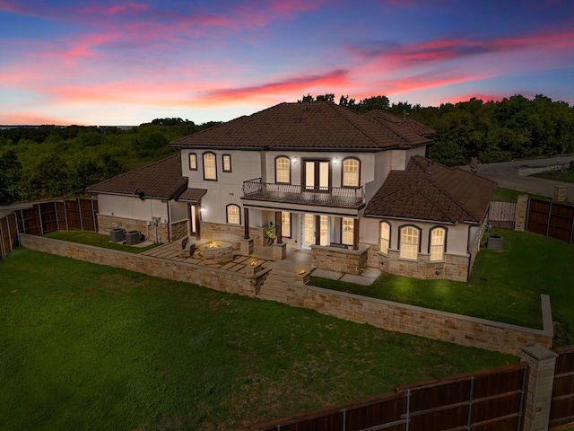 back house at dusk featuring a balcony, a fire pit, a lawn, central AC, and a patio area