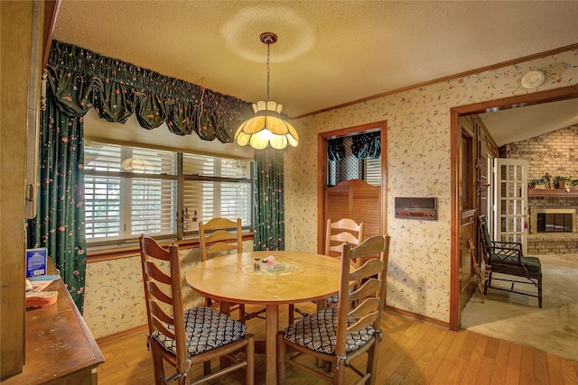 dining space with light wood-type flooring, a textured ceiling, lofted ceiling, a fireplace, and crown molding