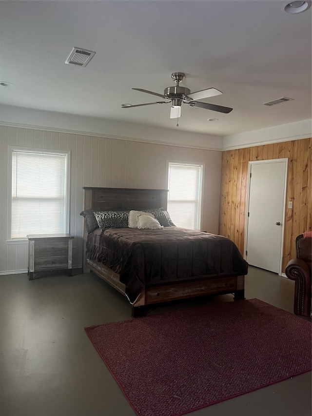 bedroom featuring ceiling fan, wooden walls, and concrete flooring