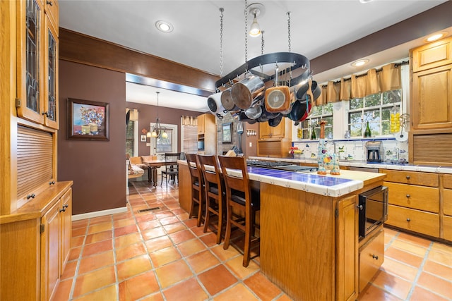 kitchen with a kitchen island, a chandelier, tile countertops, a breakfast bar, and black microwave