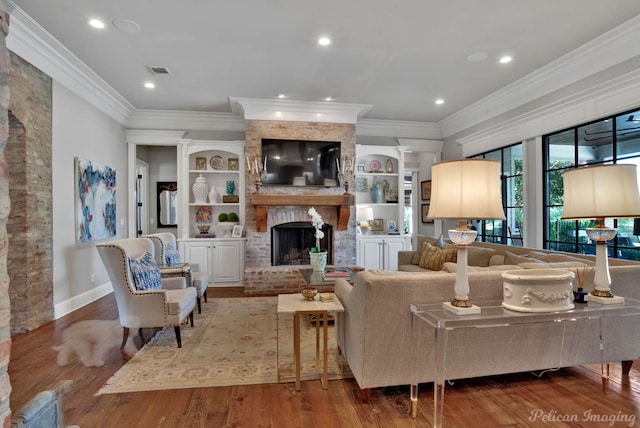 living room with built in shelves, ornamental molding, a brick fireplace, and hardwood / wood-style flooring