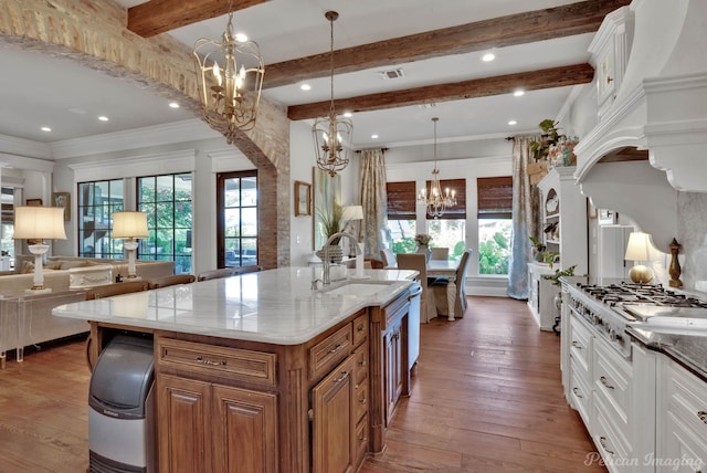 kitchen with dark wood-type flooring, sink, an island with sink, a notable chandelier, and white cabinetry