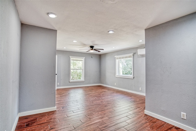 spare room featuring a textured ceiling, wood-type flooring, an AC wall unit, and ceiling fan