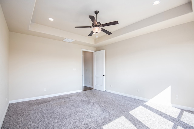 empty room with carpet, a tray ceiling, and ceiling fan