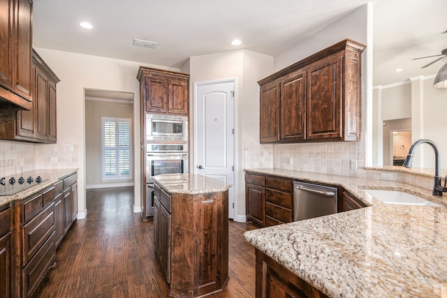 kitchen featuring appliances with stainless steel finishes, light stone countertops, a center island, ceiling fan, and dark hardwood / wood-style floors