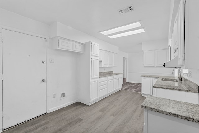 kitchen featuring white cabinets, light wood-type flooring, sink, and light stone countertops