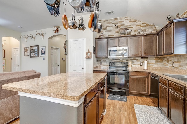 kitchen featuring vaulted ceiling, backsplash, stainless steel appliances, light wood-type flooring, and a center island