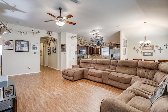 living room with ceiling fan with notable chandelier, vaulted ceiling, and light hardwood / wood-style flooring