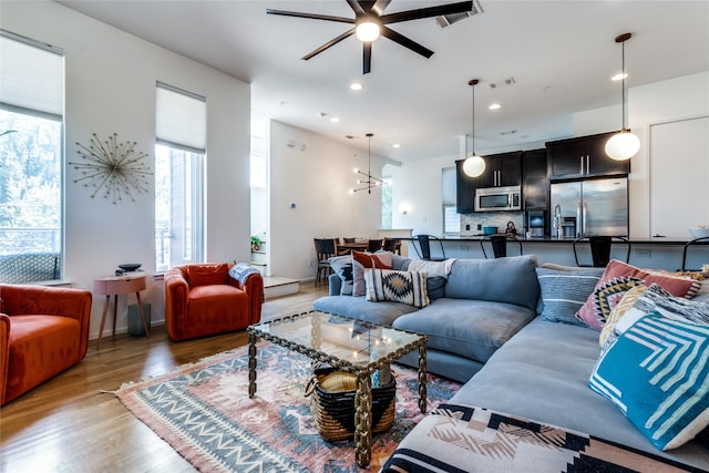 living room with ceiling fan with notable chandelier, light wood-type flooring, and plenty of natural light