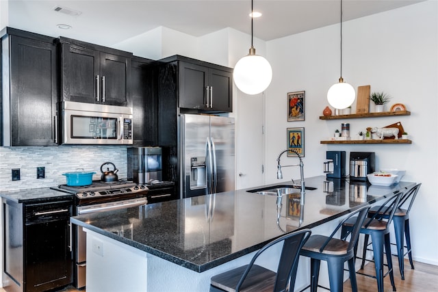 kitchen with appliances with stainless steel finishes, a center island with sink, sink, and a kitchen breakfast bar