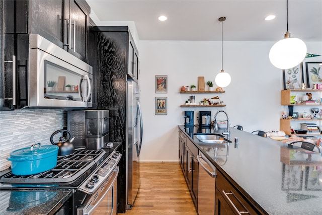 kitchen featuring appliances with stainless steel finishes, decorative backsplash, light hardwood / wood-style floors, decorative light fixtures, and sink