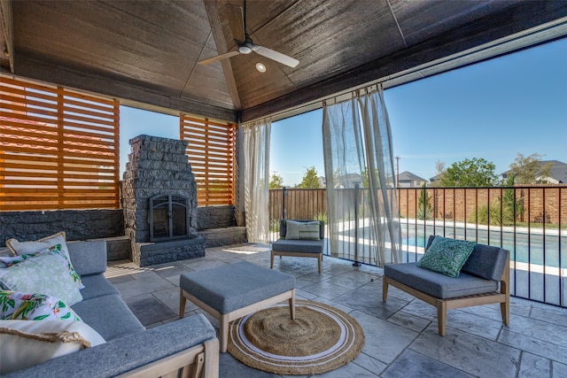 unfurnished sunroom with ceiling fan, lofted ceiling, wooden ceiling, and an outdoor stone fireplace