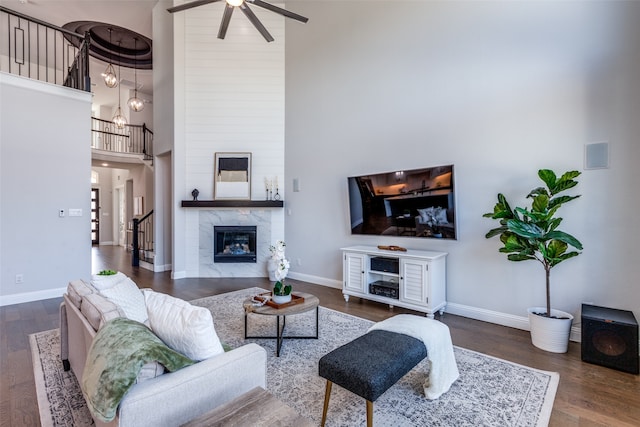 living room with ceiling fan, dark hardwood / wood-style floors, a high ceiling, and a large fireplace