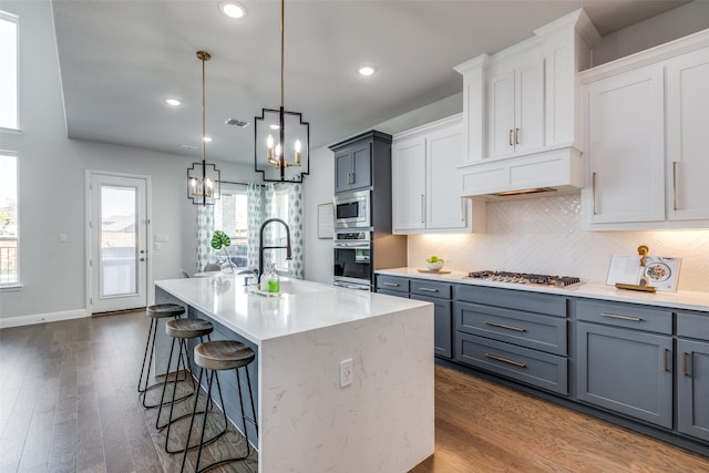 kitchen with appliances with stainless steel finishes, an island with sink, white cabinets, decorative light fixtures, and sink