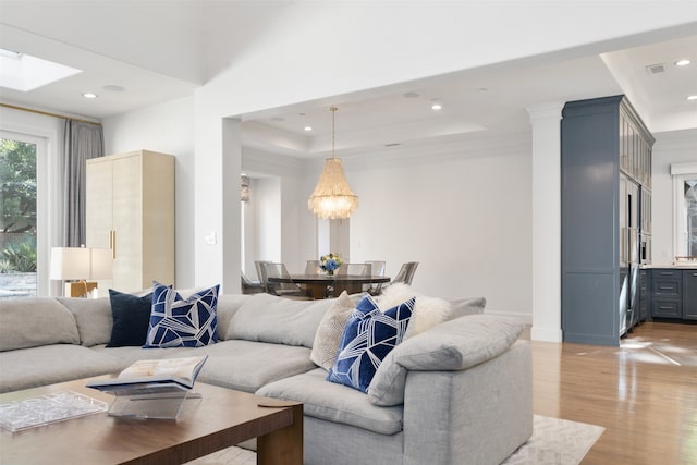 living room with a raised ceiling, crown molding, light hardwood / wood-style floors, and an inviting chandelier