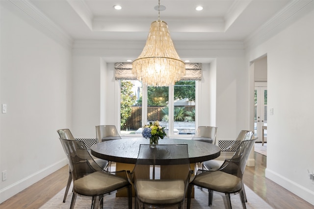 dining space featuring a raised ceiling, wood-type flooring, ornamental molding, and a chandelier