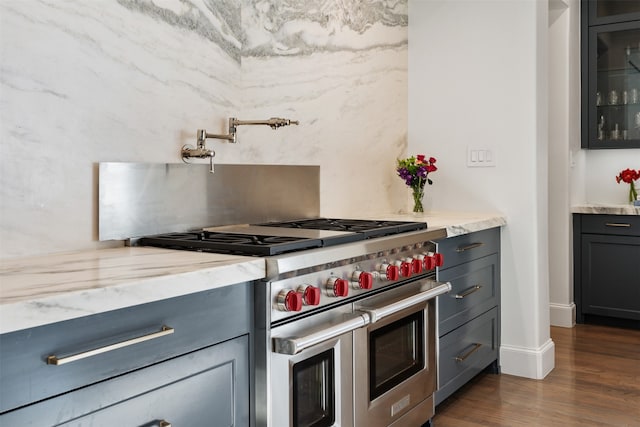 kitchen with gray cabinetry, light stone counters, double oven range, and dark hardwood / wood-style floors